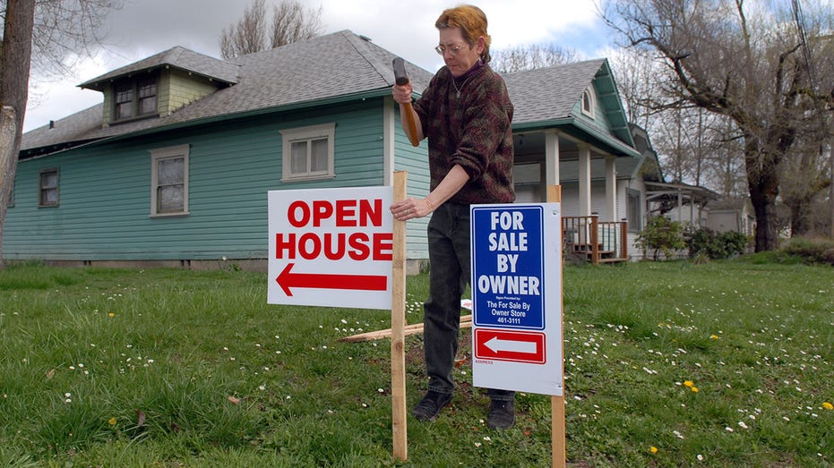 A woman hammers an open house signs into the ground in front of a home in Oregon.